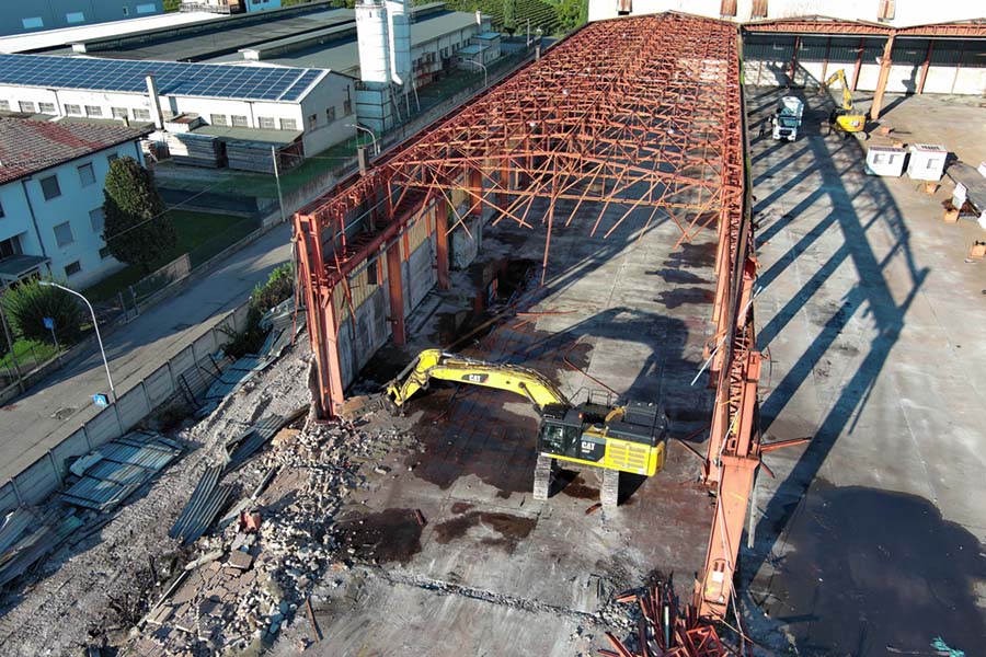 vista aerea dello scheletro metallico della fabbrica semi demolita mentre il cingolato lo distrugge