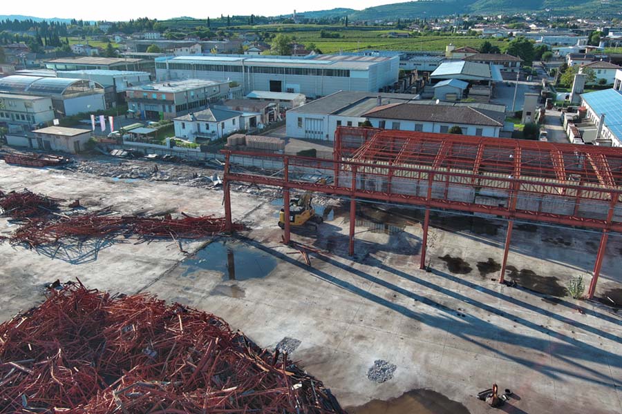 vista aerea laterale dello scheletro metallico della fabbrica semi demolita mentre il cingolato lo distrugge