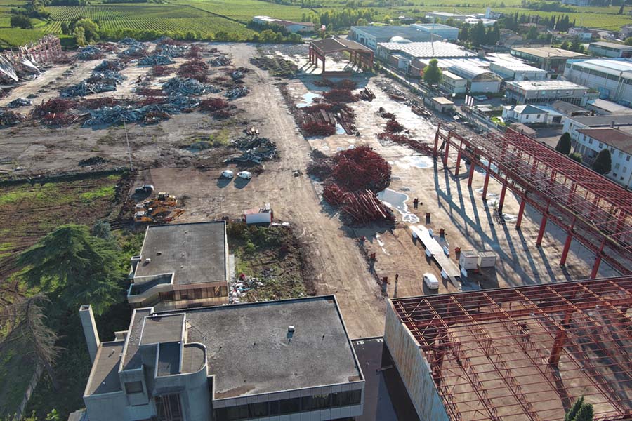 vista aerea di edifici circostanti e degli scheletri metallici della fabbrica semi demoliti mentre il cingolato li distrugge