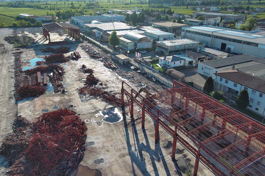 vista aerea degli scheletri metallici della fabbrica semi demoliti mentre il cingolato li distrugge