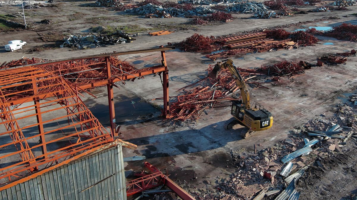 cingolato da demolizione accanto a cumuli di detriti ed a ciò che rimane dello scheletro della ex fabbrica